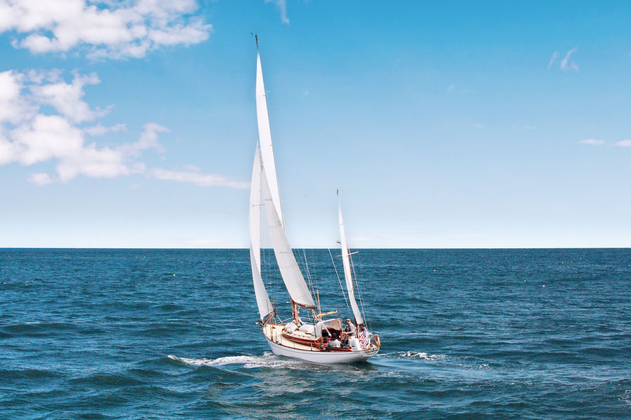 Sailboat with white sails glides on the ocean under a bright blue sky with scattered clouds. Serene atmosphere.